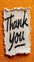 Handwritten thank you note on textured paper against a bright orange background photo