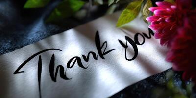Handwritten thank you note surrounded by flowers on a textured surface in soft natural light photo
