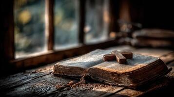 Old Bible resting on a wooden table with a cross in a dimly lit room during the early morning photo