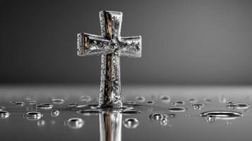 Silver cross standing on a reflective surface with droplets of water around it photo