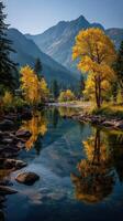 Majestic autumn scene with vibrant yellow trees reflecting in calm river surrounded by mountains during midday photo
