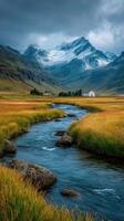 Snow-capped mountains rise above a tranquil stream flowing through golden fields at dusk photo