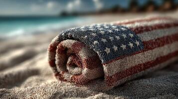 Towel with an American flag design resting on the sand at a beach during a sunny day photo