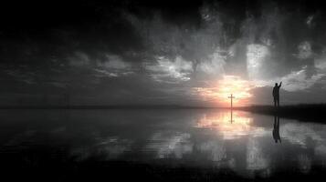 Silhouette of a person worshipping at sunset by the water with a cross reflection photo