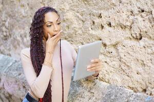 A surprised woman is looking intently at a tablet while in a bustling urban setting photo