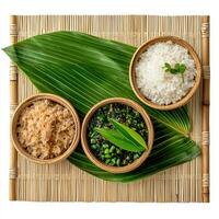 Three bowls of rice, green vegetables and a leaf on a bamboo mat photo