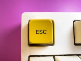 Large yellow Esc button on a white keyboard, on a purple background, flay lay, copy space photo