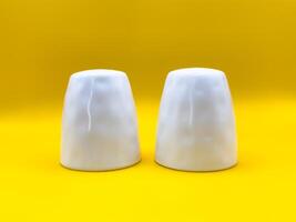 Two white ceramic salt and pepper shakers on a yellow background in the center of the image, top view photo