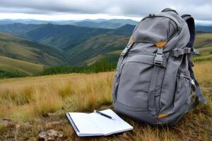 Backpack and notebook resting on mountain meadow overlooking scenic valley photo
