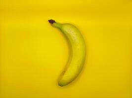 One bright yellow banana on a yellow background in the center of the image, top view photo