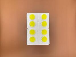 Yellow cough tablets in silver packaging on beige background, top view photo