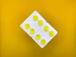 Yellow tablets in silver packaging on yellow background in the center of the image, top view photo