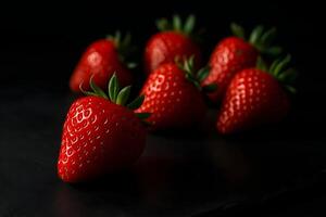 Vibrant red strawberries on a dark matte black slate surface with dramatic lighting and subtle reflections. photo