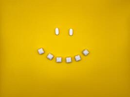 Smiley face with eyes and smile made from chewing gum and pills on yellow background, top view photo