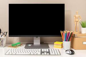 Workspace showing computer with black blank screen, keyboard, mouse and various stationery items, ideal for designers, students or creative workers. Template mockup photo