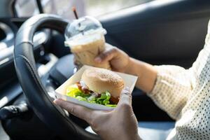 woman driver hold and eat hamburger in car, dangerous and risk an accident. photo