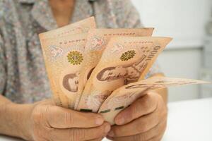 senior woman patient holding Thai banknotes money in her hand, Cost of living and medical care. photo
