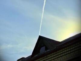 thin plane trail in blue sky above triangular roof, geometric shape in sunlight photo