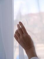 female hand against the background of a window curtained with transparent fabric, copy space photo