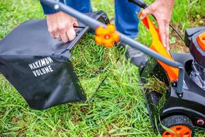 Mowing grass with a petrol lawn mower in spring. The man detached the container with the mown grass to put it in the compost photo