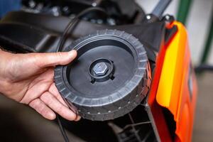 Assembling a petrol lawn mower. A man attaches a plastic wheel to the body of the lawn mower photo