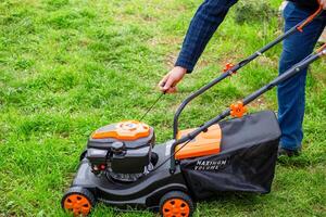 A man starts the engine of a petrol lawn mower with a starter rope. Mowing grass in the spring in a garden plot. photo