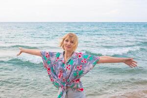 Woman standing on beach with open arms and contented expression. Happy summer vacation at sea. photo