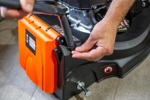 Assembling a petrol lawn mower. A man secures the drive control handle with a bolt photo