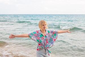 Woman standing on beach with open arms and contented expression. Happy summer vacation at sea photo