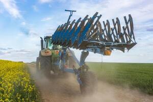 A tractor pulls a plow through a dirt road flanked by blooming yellow flowers in a vast green field under a bright sky photo