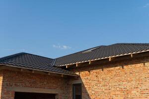 A newly finished brick house features a sleek black tiled roof under a clear sunset sky with scattered clouds, highlighting modern architecture photo