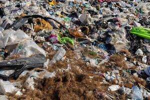 A large area of a landfill site covered with various types of waste such as plastic, fabric, and organic materials during daylight hours photo