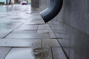 Water drips from a drain pipe onto slick pavement, showing the aftermath of rain in an urban environment photo