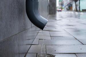 Water continuously drips from a downspout onto the pavement creating small puddles in a city after rain photo