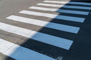 Crosswalk lines create a clear path for pedestrians in a city setting, illuminated by natural sunlight in late morning photo