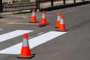 Brightly colored safety cones and a broom lie near freshly painted street lines under clear skies, indicating ongoing road work photo