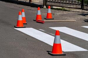 Traffic cones surround a freshly painted pedestrian crossing in a busy urban street during daytime, ensuring safety during repainting photo