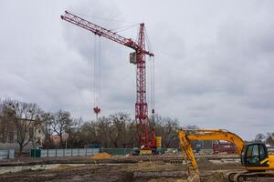 A large red crane stands at a construction site with heavy machinery working amid overcast weather, indicating ongoing building activity photo