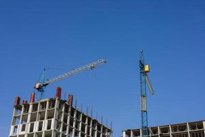 Construction cranes tower over a building site where workers are engaged in various tasks during a sunny afternoon photo
