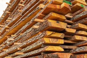 Wooden planks are neatly stacked in a woodworking space, revealing unique textures and colors, illuminated by natural light coming through the window photo