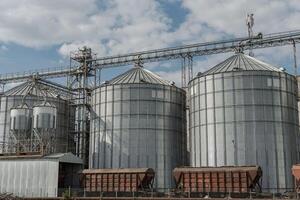 Large metallic silos feature prominently at a grain storage facility amidst a cloudy sky and scattered fields photo