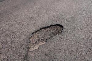 Recent heavy rain has left a substantial footprint-shaped mark in the asphalt of a city street, showing the effects of weather on infrastructure photo