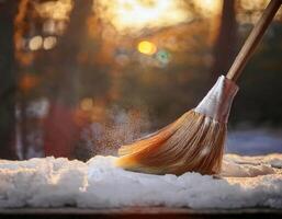 A simple broom moves through powdery snow at dusk, its bristles pushing aside the cold layers as the fading sunlight casts a soft golden shimmer over the winter scene. photo