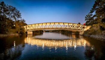 Bridge illuminated over a calm river at twilight. Lights reflect on the water. A peaceful urban scene. Explore the bridge's architecture. photo