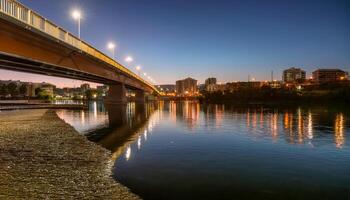 Bridge illuminated over a river at twilight, city lights reflecting on the water. Urban cityscape with buildings along the shore. Tranquil evening scene. photo