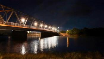 Bridge illuminated at night, lights reflecting on the dark river below. Truss structure spans the water. Tranquil and serene urban scene. Explore the night lights and reflections. photo