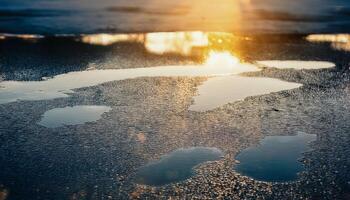 Puddles of water reflecting the golden light of the setting or rising sun and the sky. Wet asphalt surface. Abstract and atmospheric view capturing the shimmering reflections. photo