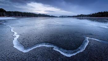 Wide view of a frozen lake with a prominent crack in the ice, under an overcast and moody sky. Winter landscape with trees lining the distant shore. Captures the cold stillness photo