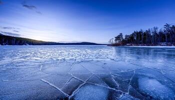 Wide view of a cracked ice surface on a frozen lake at twilight, with a deep blue sky and trees lining the shore. Winter landscape capturing the cold beauty and the stillness of the evening. photo