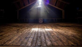 Empty wooden stage floor illuminated by a bright spotlight from above, with visible rafters and a dark backdrop. Evokes anticipation and the potential for performance in a rustic setting. photo